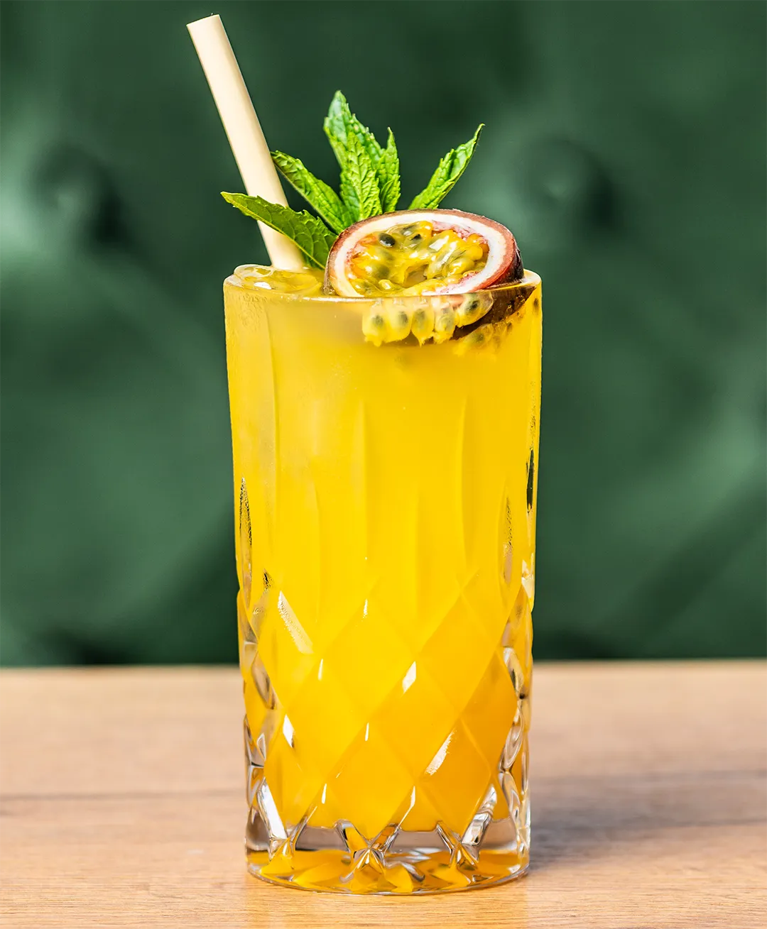 Eiskalte gelbe Maracuja-Limonade in einem Kristallglas, garniert mit einer halben Passionsfrucht, Minze und Strohhalm auf einem Holztisch.