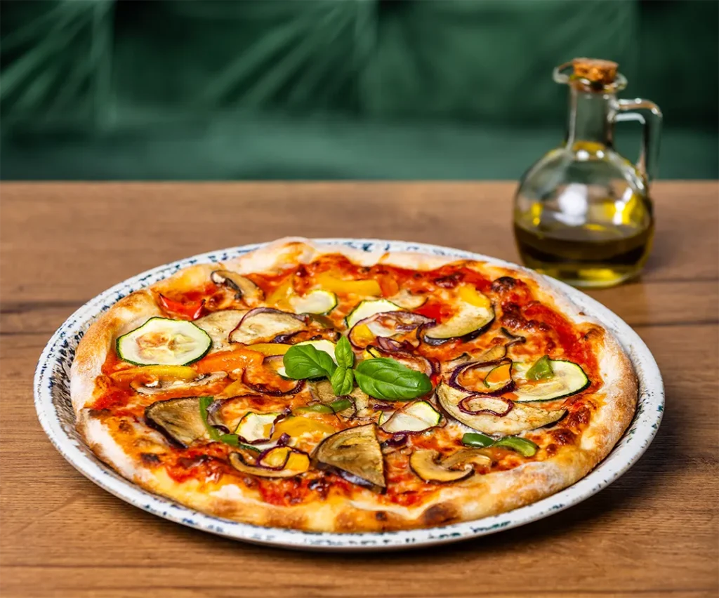 Frische vegetarische Pizza belegt mit Zucchini, Auberginen, Paprika, Champignons und Basilikum auf einem Holztisch.
