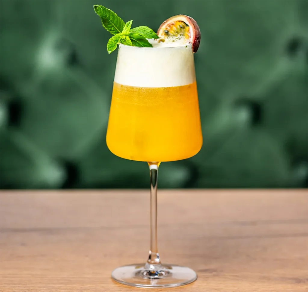 Fruchtiger Lillet Maracuja Spritz im Stielglas mit weißer Schaumkrone, garniert mit Passionsfrucht und frischer Minze.