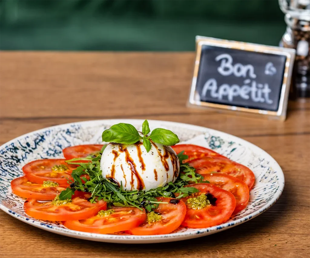 Italienische Vorspeise Caprese mit frischer Burrata, Tomatenscheiben, Rucola, Pesto und Balsamico-Glaze.